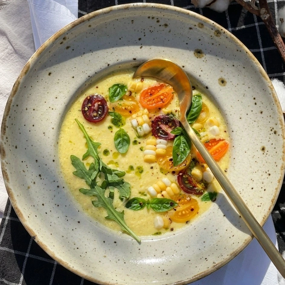 A bowl of golden Sweet Corn Gazpacho with basil oil and corn.