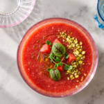 A bowl of golden Tomato Watermelon Gazpacho with basil oil and nuts.