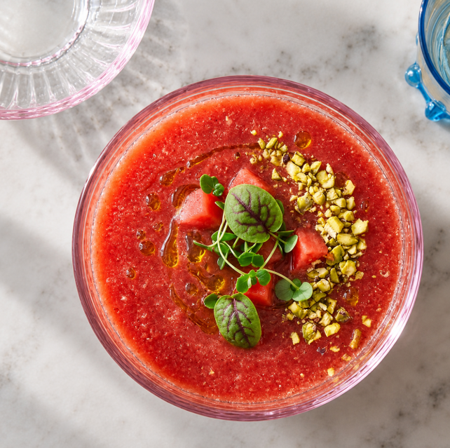 A bowl of golden Tomato Watermelon Gazpacho with basil oil and nuts.